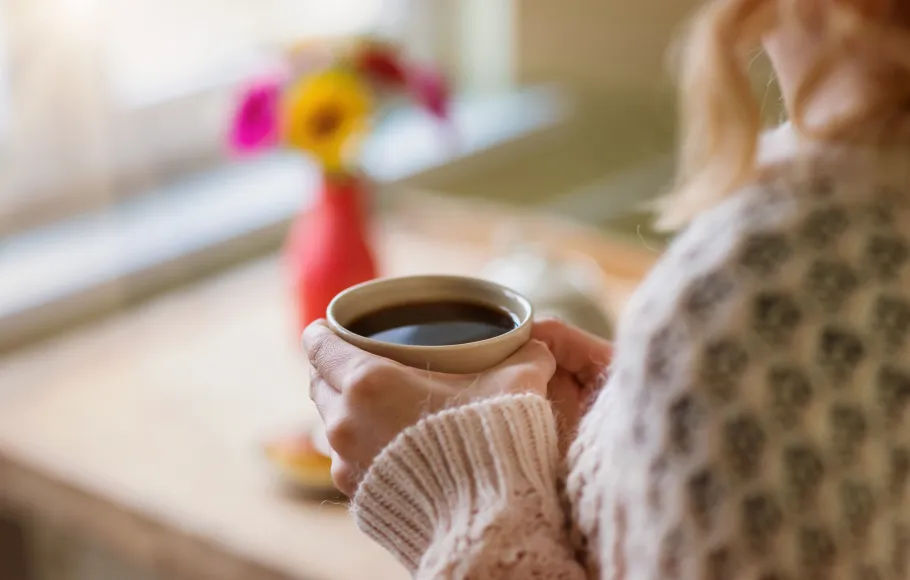Kvinna står och tittar ut genom fönster med en kaffekopp