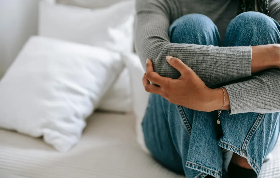 Kvinna sitter hopkurad i en säng