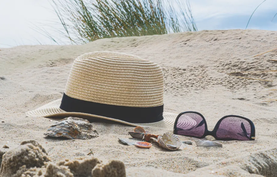 En bild på solglasögon och en sommarhatt liggandes på en strand