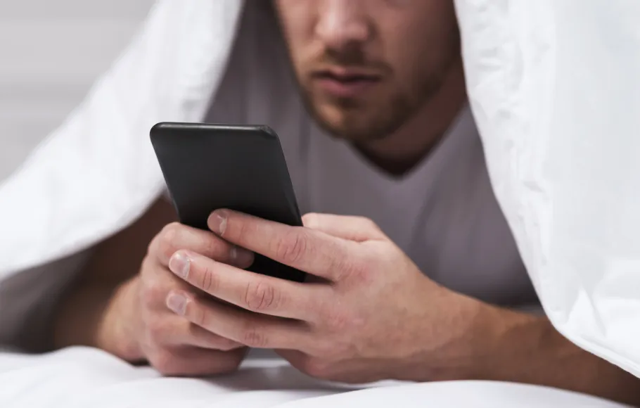 Man under täcker som kollar i sin mobil