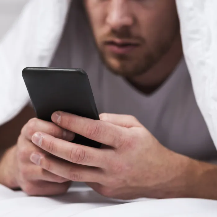 Man under täcker som kollar i sin mobil